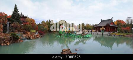 Chinese Garden with waterfall and colorful figurines reflected on water, Chinese Pavilion and Stadium tower Stockfoto