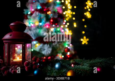 Rote Laterne mit Kerze und Weihnachtsdekoration vor einem beleuchteten Baum Stockfoto
