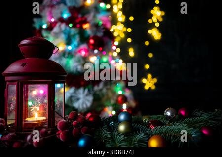 Rote Laterne mit Kerze und Weihnachtsdekoration vor einem beleuchteten Baum Stockfoto