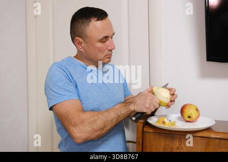 Mans Hände schälen einen Oma smith Apfel. Ein erwachsener Mann steht an der Tür und schält eine Birne auf einen Teller Stockfoto