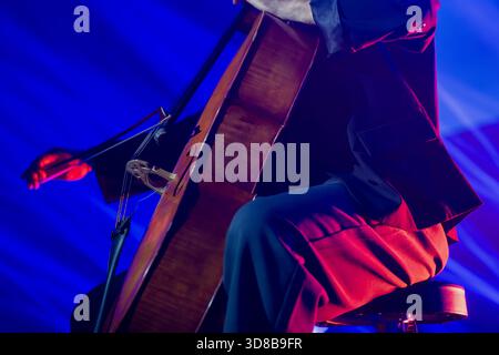 Cellist tritt auf der Bühne mit starken blauen Lichtstrahlen auf, die das Instrument beleuchten und warme Highlights über den Anzug des Musikers werfen Stockfoto