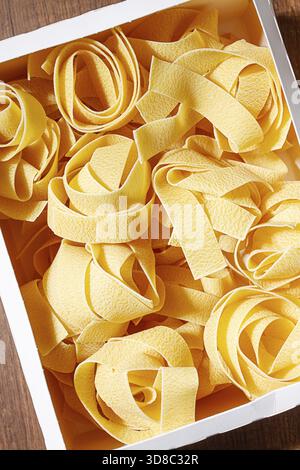 Rohe Pappardelle Nudeln, Nudelnester, in einem Papierkarton, hartes Licht, Blick von oben, keine Leute Stockfoto