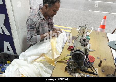 Little India, Singapur, 9. September 2025 männlicher Handwerker repariert ein weißes Kleidungsstück, während seine Nähmaschine in einer Kleiderwerkstatt stillsteht Stockfoto