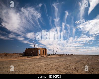 Die Hülle eines alten Gebäudes an der Seite einer Straße mit bewölktem Himmel im australischen Outback Stockfoto