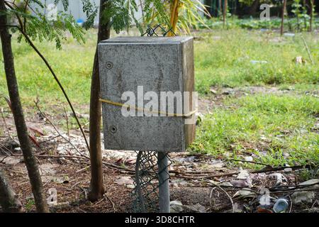 Rustikaler Schaltkasten für den Außenbereich mit Seil und Maschendrahtzaun in naturgrüner Umgebung gesichert. Fördert Sicherheit, Versorgungseinrichtungen und ländliche Infrastruktur. Stockfoto