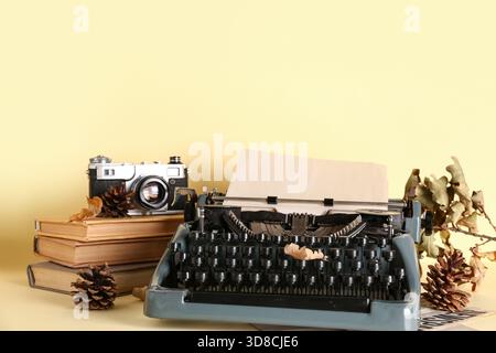 Vintage Schreibmaschine, Bücher, Tannenzapfen, Fotokamera und Herbstblätter auf gelbem Hintergrund Stockfoto
