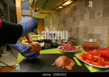 Mit Handschuhen gefüllte Hände mit Zwiebeln und gehacktem Pfeffer, Mischen mit gemahlenem Fleisch auf Schneidebrett, bereiten Schüsseln und Utensilien vor Stockfoto