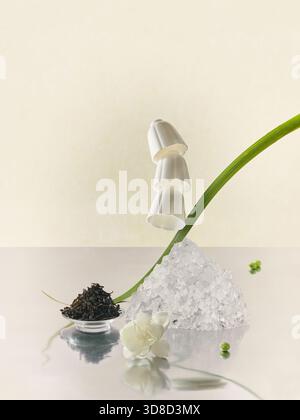 Surreale Zusammensetzung fallender weißer Teetassen über Eiskristalle mit trockenen Teeblättern und Jasminblüten Stockfoto