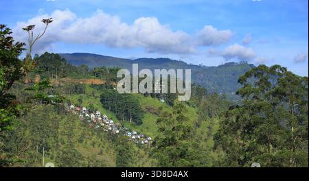 Malerische Landschaft Blick auf eine Bergkette in den Highlands von ri Lanka, mit einem kleinen Dorf eingebettet in den Hügel. Es gibt einen schönen blauen, bewölkten Himmel Stockfoto