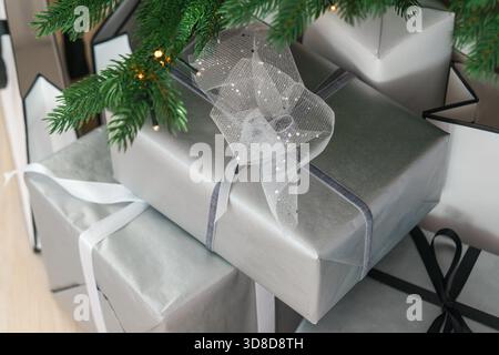 Stilvolle Weihnachtsgeschenkboxen mit silbernem Papier, Geschenke mit zarten Bändern unter einem verzierten Weihnachtsbaum. Warme Lichter sorgen für den Winter Stockfoto