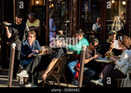Paris, Frankreich - Mai 2025: Die Besucher genießen an einem lebhaften Abend Drinks und Gespräche in der Bar Le Progres in Montmartre. Die untergehenden Sonnenstrahlen reflektieren Stockfoto