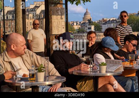 Paris, Frankreich - Juni 2025: Besucher treffen sich an Tischen vor dem Café des Arts am seine-Ufer in Paris. Die Kuppel des Panthéons erhebt sich in der B Stockfoto