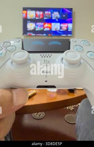 Doha, Katar - 28. November 2025: Ein Spieler spielt zu Hause Play Station 5, seine Hand hält den Dual Sense Joystick, den neuen Wireless Controller. Stockfoto