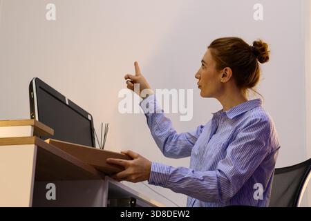 Junge Frau in blau gestreiftem Hemd greift das Paket mit einer Hand, während sie den Finger nach oben zeigt. Stockfoto