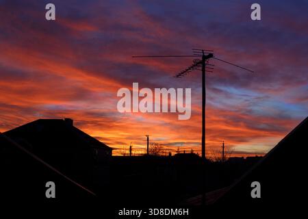 Ein heller Sonnenuntergang über den Umrissen von Häusern und eine Fernsehantenne gegen den Himmel. Stockfoto
