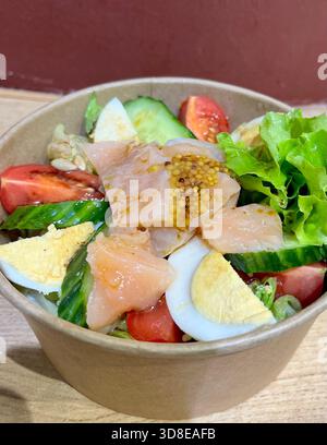 Geräucherter Lachs, gekochtes Ei und frischer Gemüsesalat in der Poke-Schüssel aus Papier, Café zum Mitnehmen von Gemüse und Lachssalat Stockfoto