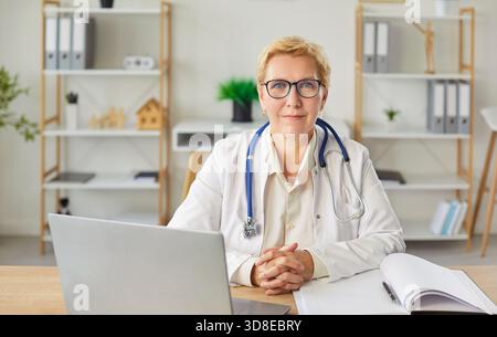 Reife Ärztin lächelt am Schreibtisch, medizinische Beraterin, weibliche medizinische Krankenschwester oder Praktikerin Stockfoto