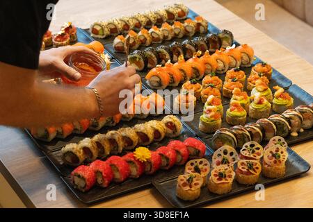 Eine Person spritzt elegant Sauce auf eine luxuriöse, große Gourmet-Platte mit verschiedenen Sushi-Brötchen, einschließlich Lachs, rotem Kaviar und essbarem Goldtoppin Stockfoto