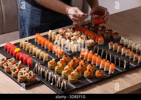 Eine Person spritzt elegant Sauce auf eine luxuriöse, große Gourmet-Platte mit verschiedenen Sushi-Brötchen, einschließlich Lachs, rotem Kaviar und essbarem Goldtoppin Stockfoto