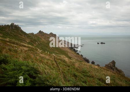 Zerklüftete Landzunge an der Küste mit grasbewachsenen Hängen und felsigen Felsvorsprüngen mit Blick auf das ruhige Meer unter einem bewölkten Himmel. Stockfoto