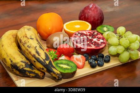 Bunte frische Obstplatte mit Kochbananen, Granatapfel, Kiwi, Beeren, Orange, Trauben, für gesunde Ernährung Stockfoto