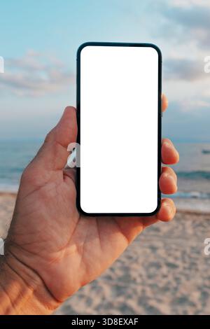 Handheld-Smartphone mit leerem Bildschirm am Strand bei Sonnenuntergang, Präsentation von Apps, Webdesign oder Benutzeroberfläche in natürlicher Umgebung im Freien. Selektiver Fokus. Stockfoto