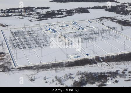 Blick von oben auf ein großes Umspannwerk in einer schneebedeckten Winterlandschaft. Elektrische Infrastruktur für Energieverteilung und -Übertragung. Stockfoto