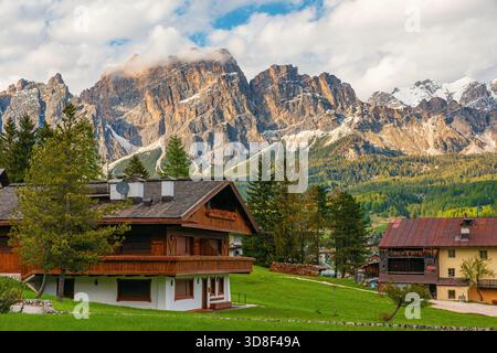 Charmante Almhütten aus Holz in Cortina d'Ampezzo mit grünen Wiesen und schneebedeckten Dolomitenbergen. Italienische Dolomiten in Belluno Stockfoto