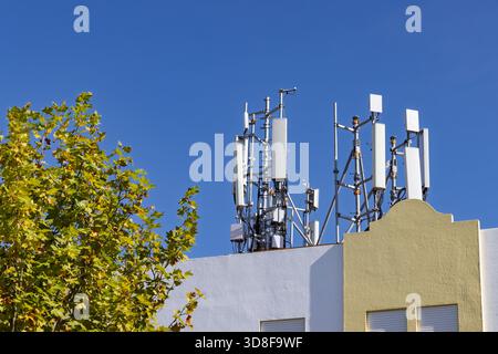 Kommunikationsantennen und Mobilfunkmasten für 5G-, 4G- und spätere 6G-Datenübertragung auf einem Gebäudedach vor klarem blauem Himmel. Stockfoto