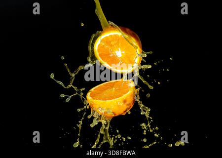 Frisch geöffnete Orangenfrüchte mit Orangensaftspritzern auf schwarzem Hintergrund. Stockfoto