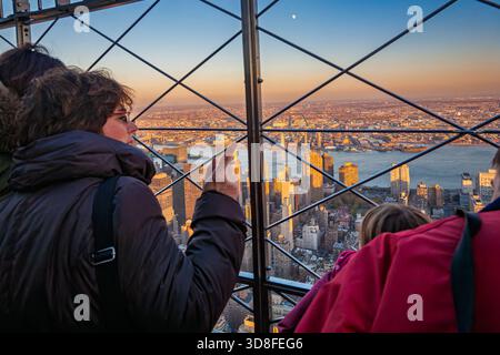 Bei Sonnenuntergang genießen Besucher die leuchtende Skyline von Midtown Manhattan und den East River von der Aussichtsplattform des Empire State Building aus. Stockfoto