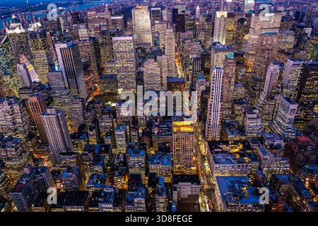 Der Blick aus der Höhe auf Midtown Manhattan zeigt lebhafte Wolkenkratzer, die bei Nacht leuchten, vom Aussichtspunkt des Empire State Building aus gesehen. Stockfoto