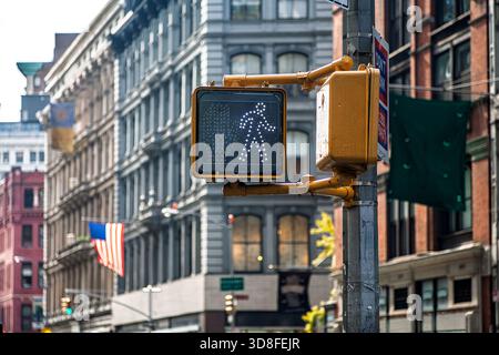 Ein Fußgängersignal leuchtet grün auf dem Broadway, New York City. Nahe gelegene Gebäude schaffen eine lebendige urbane Kulisse unter blauem Himmel. Stockfoto