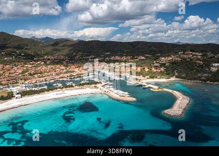 Blick aus der Vogelperspektive auf eine Hafenstadt entlang des klaren türkisfarbenen Wassers, mit einem geschützten Yachthafen, Sardinien, Italien Stockfoto