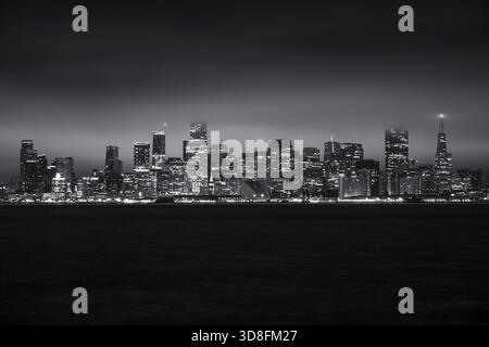 Panoramablick bei Nacht auf die beleuchtete Skyline von San Francisco und die Bay Bridge über dem Wasser. Stockfoto
