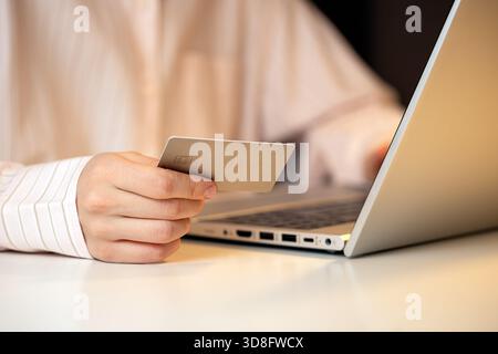 Nahaufnahme einer Person, die eine Kreditkarte hält, während sie einen Laptop verwendet, und die Online-Shopping, digitale Zahlungen und sichere Internettransaktionen darstellt Stockfoto