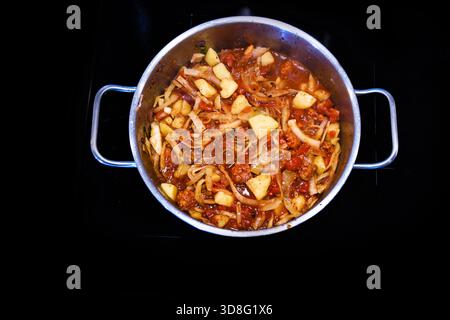 Kohl-Eintopf oder Suppe mit Kartoffeln, Chorizo-Wurst und Tomaten in einem Kochtopf auf dem schwarzen Herd, hausgemachtes Essen für eine große Familie oder eine Party, Stockfoto