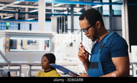 Porträt eines Ingenieurs in der Photovoltaik-Fabrik, der Papiere zur Diagnose von Systemfehlern überprüft. Mitarbeiter von Solarpaneelen lesen Inspektionsdatendateien, um Ausfallzeiten zu reduzieren. Kamera B.. Stockfoto