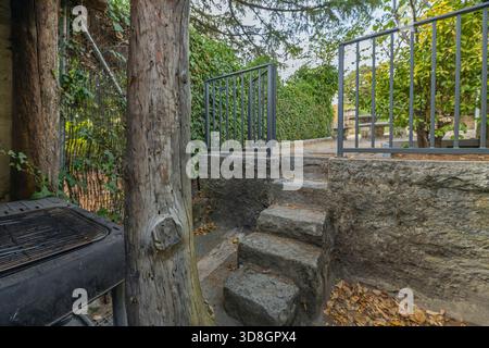 Ein Seitenkorridor mit Granitplatten und einer teilweise mit Efeu bedeckten Natursteinmauer integriert die Vegetation in die Architektur Stockfoto