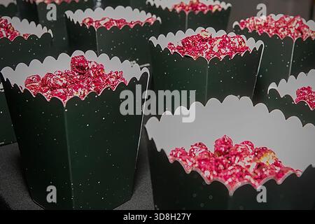 Nahaufnahme mehrerer Popcorn-Boxen aus schwarzem Papier, gefüllt mit hellrotem Karamell-Popcorn. Festliche, farbenfrohe Snackpräsentation in Reihen angeordnet, geeignet Stockfoto