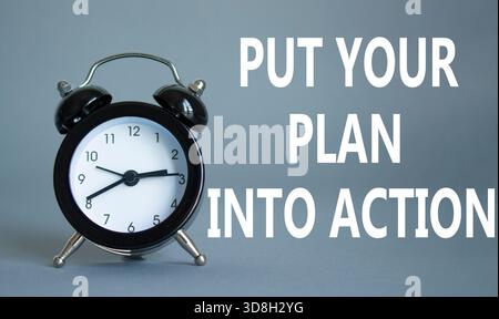 Setzen Sie Ihren Plan in die Tat um. Konzeptworte setzen Ihren Plan auf weißes Puzzle in die Tat um. Schöner grauer Hintergrund mit Wecker. Business Conep Stockfoto
