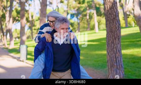 Verspieltes Seniorenpaar, das Spaß mit einem Huckepack-Ritt hat Stockfoto