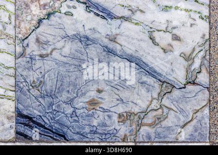 Nahaufnahme von alten und strukturierten Marmorfliesen mit komplexen Mustern aus blauen und grünen Adern auf weißem und hellgrauem Grund, die Anzeichen von Verschleiß und Zeit zeigen. Stockfoto