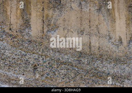 Nahaufnahme einer strukturierten Betonwand mit Anzeichen von Witterung und eingebettetem Zuschlagstoff. Vertikale Flecken laufen im oberen Teil der Wand entlang. Stockfoto