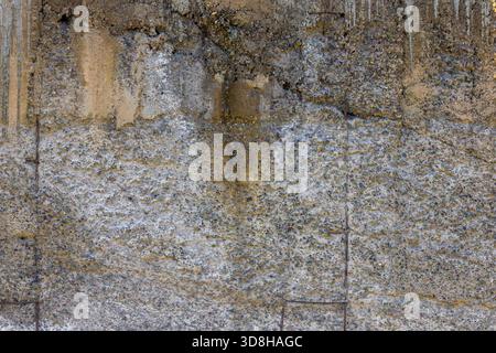 Nahaufnahme einer strukturierten Betonwand mit Anzeichen von Witterung und eingebettetem Zuschlagstoff. Vertikale Flecken laufen im oberen Teil der Wand entlang. Stockfoto