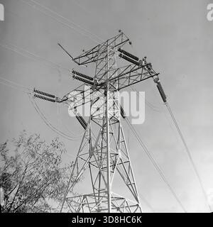 Region Donezk, ukrainische SSR, Sowjetunion. 1970er Jahre Installationsarbeiten an einem leistungsstarken Ankerwinkelträger einer 500 kV Hochspannungsleitung. Linemen arbeiten in großer Höhe an den Metalltraversen und der Turmspitze, um Isolatorseile und -Kabel zu sichern. Unten unterstützt ein Nutzfahrzeug mit einer Antennenplattform den Betrieb. Die komplexe Gitterstruktur des Pylons hebt sich vom Himmel ab. Bau des sowjetischen Energienetzes. Das Leben im friedlichen Donbass vor dem Krieg. Stockfoto