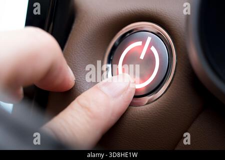 Nahaufnahme eines Fingers, der in einem modernen Fahrzeug auf einen leuchtenden Netzschalter drückt, der Kontrolle, Aktivierung, Technologie, Innovation, automotiv Stockfoto
