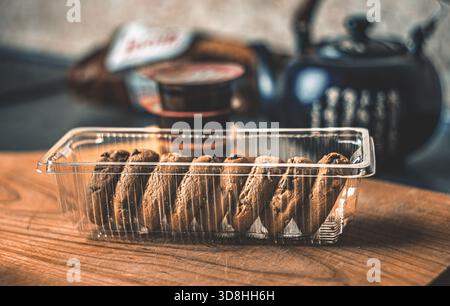 Ein rustikaler Tee-Moment in der Küche: Schwarze Teekanne aus Ton, knusprige Kekse und portionierte Marmelade auf einem Holztisch bei sanftem Tageslicht Stockfoto