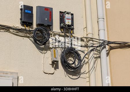 Unordentliche Installation von Glasfaser- (PDO) und Kommunikationskästen an einer Gebäudeaußenwand. Schwarze Spiralkabel und freiliegende Drähte. Stockfoto