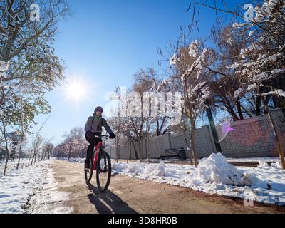 Ein Mann fährt im Winter auf einem Radweg in der Stadt. Aktiver Lebensstil im Winter. Ein erwachsener Mann auf einem roten Fahrrad mit einem Helm auf dem Kopf Stockfoto